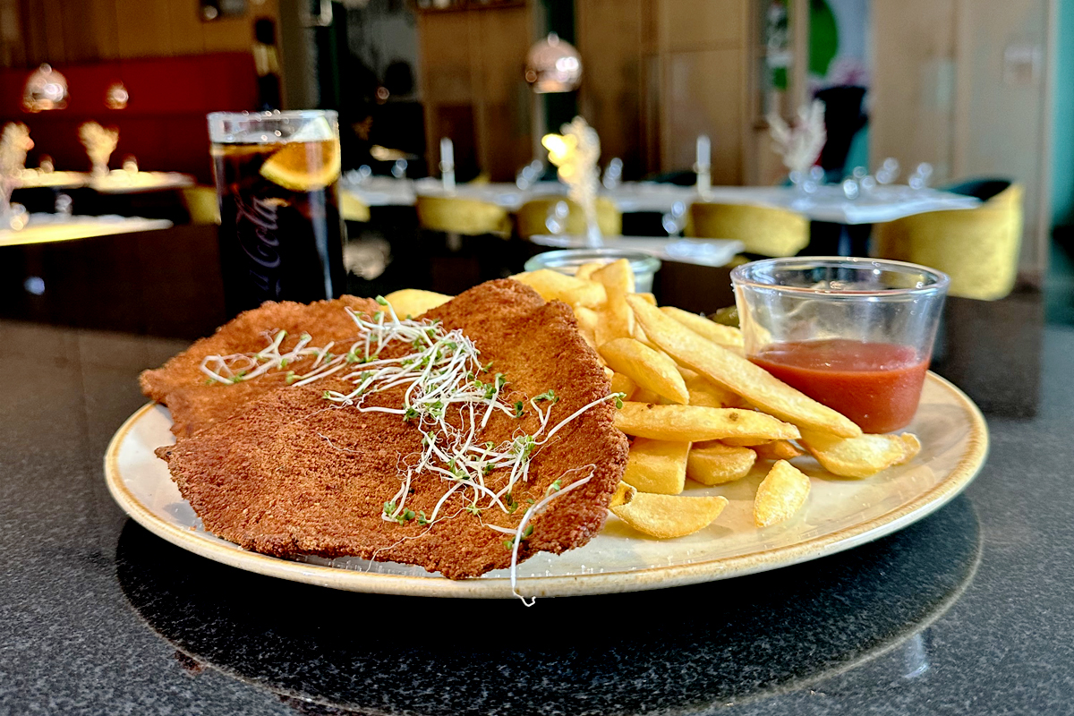 Gebratenes Schnitzel mit knusprigen Pommes frites, Soße und einem Getränk auf einem schwarzen Tisch in einem Restaurant in Teltow, Berlin-Potsdam.